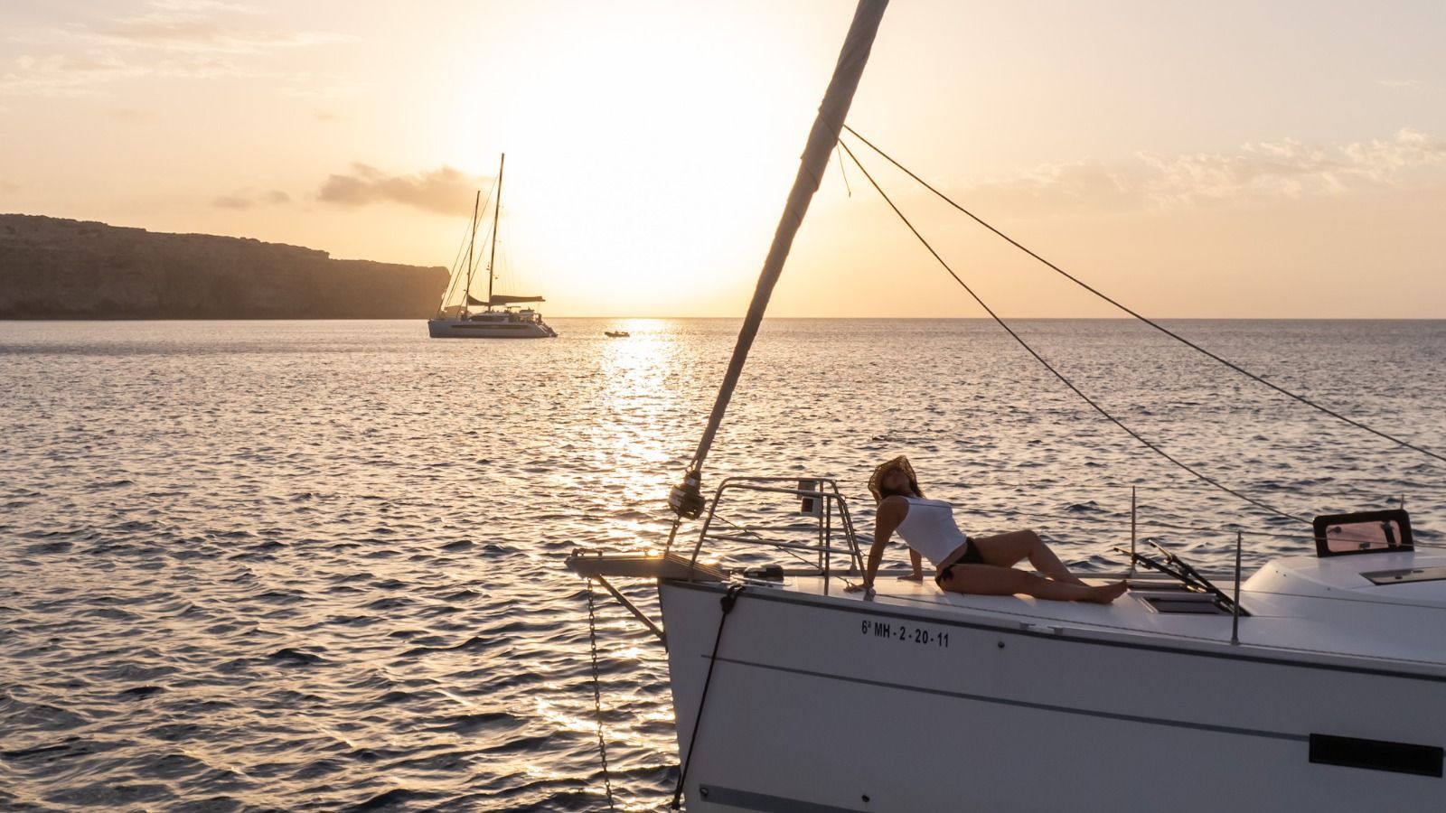 Una mujer está tumbada en un velero en el océano al atardecer.