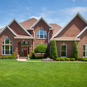 Brick suburban house with manicured green lawn and blue sky