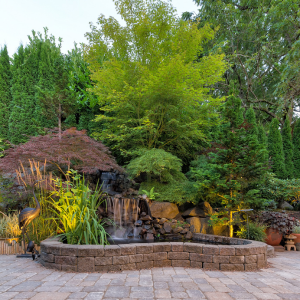 Landscaped garden with a small waterfall, pond, stone wall, and lush green trees