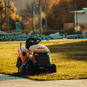 Orange riding lawn mower on grass near a paved path in a sunny yard
