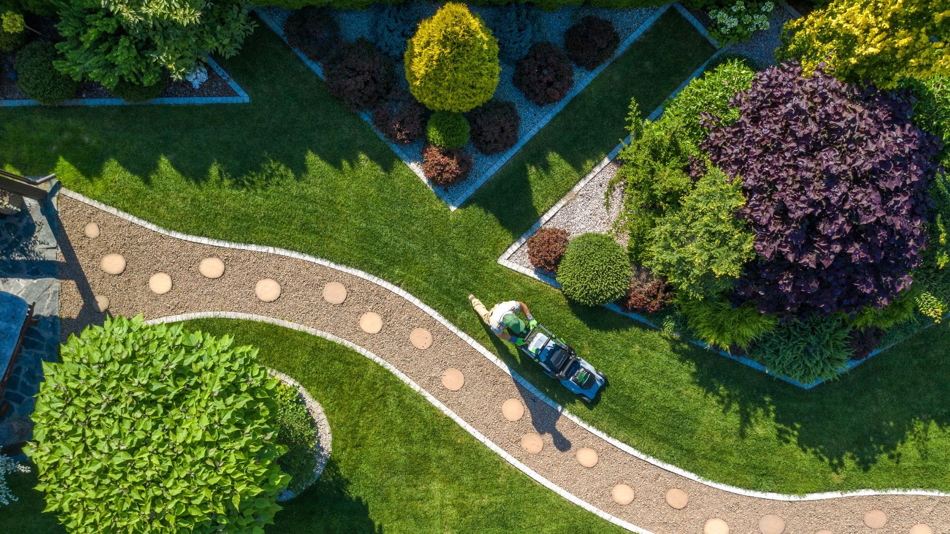Top-down view of a curved garden path with stepping stones, lush green lawns, and purple and yellow shrubs