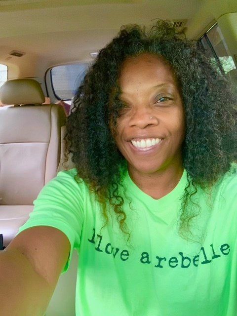 Smiling person in a green shirt taking a selfie inside a car
