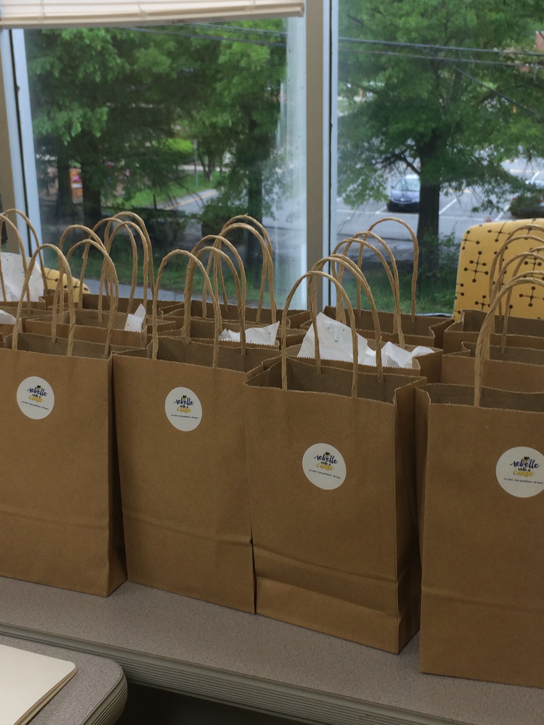 Brown paper gift bags with handles lined up on a table by a window.