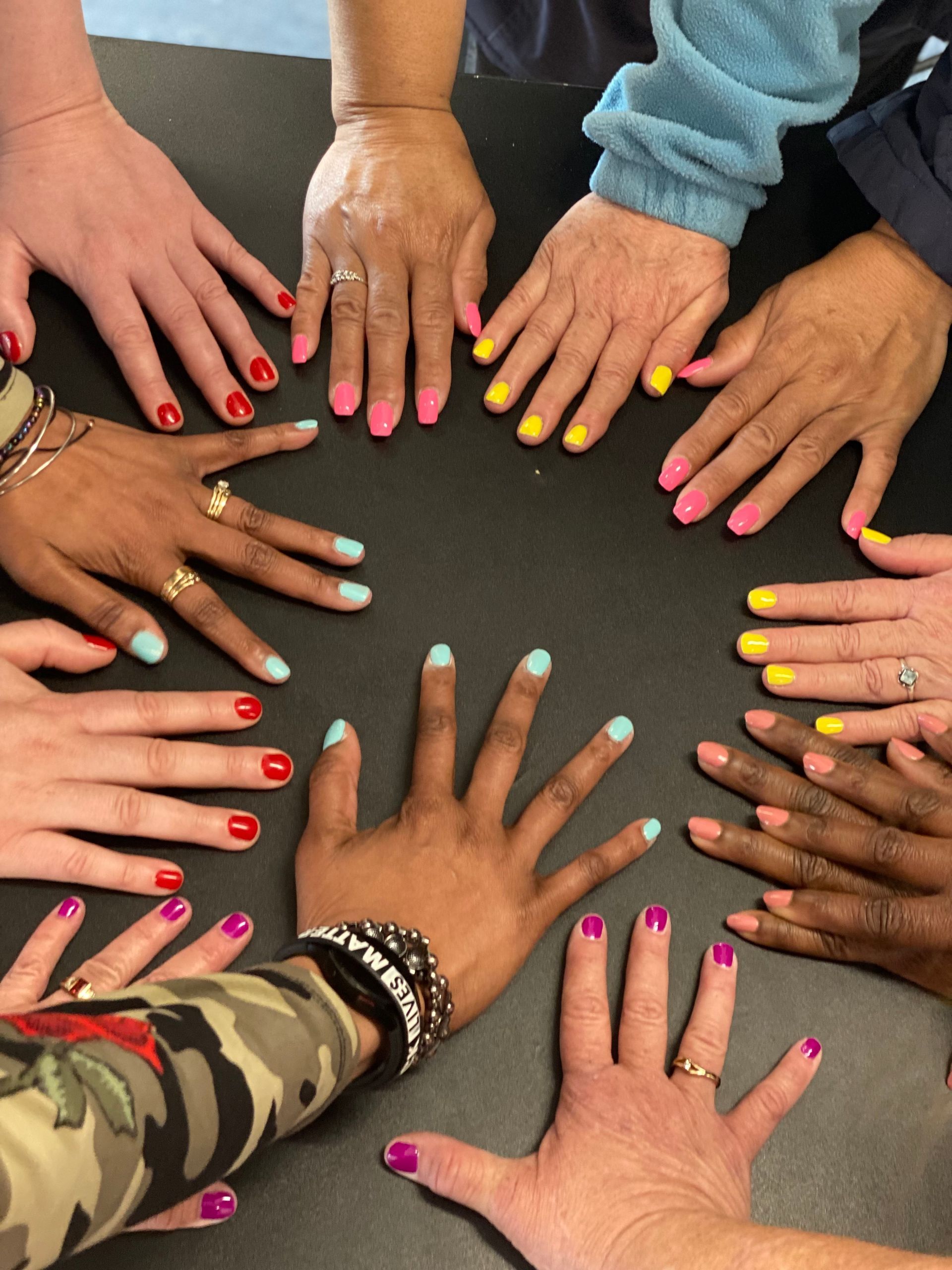 Hands with colorful painted nails arranged in a circle on a table