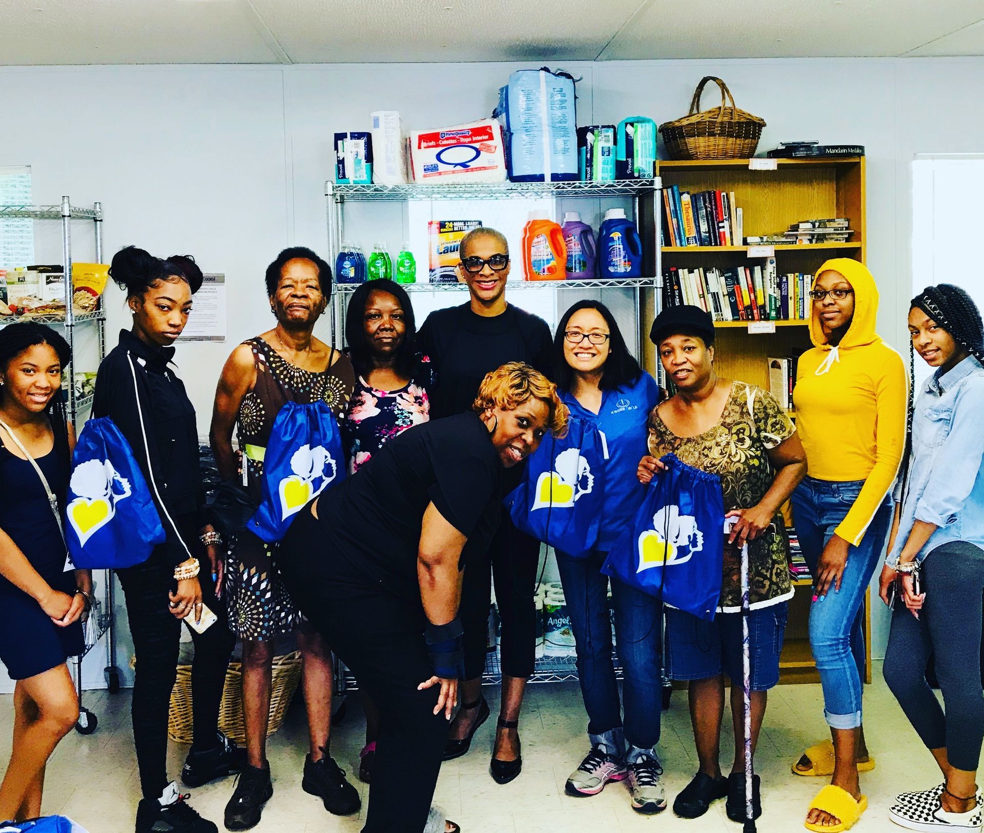 Group of people posing indoors, holding blue gift bags in front of shelves with supplies and baskets.