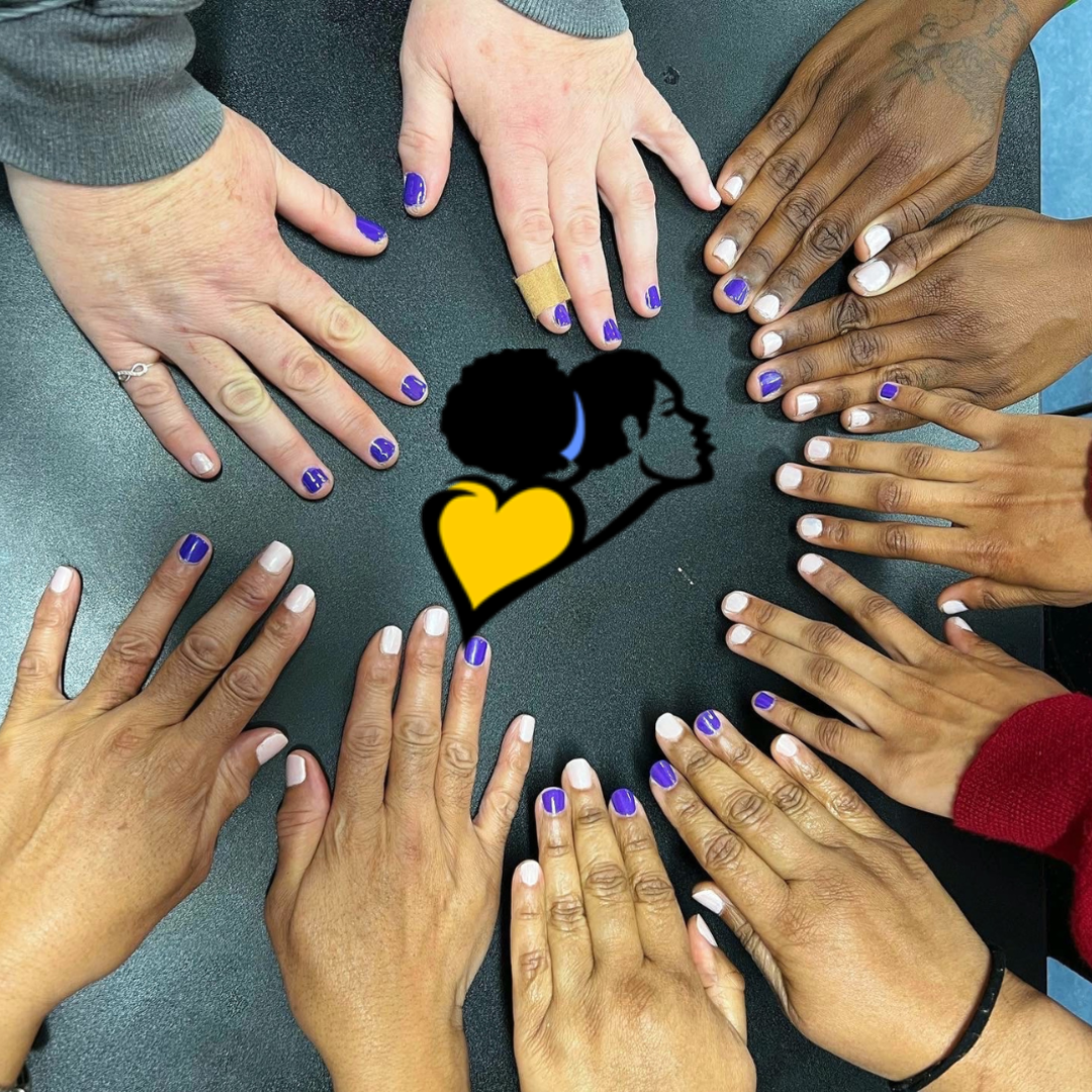 Hands with purple nail polish forming a circle around a black and yellow heart logo on pavement