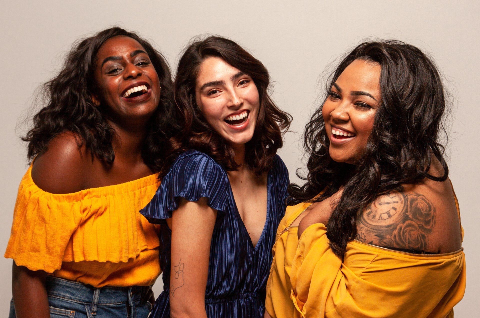 Three smiling people posing together against a light background, wearing bright orange and blue tops.
