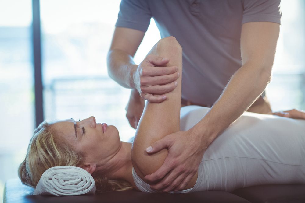 Therapist Stretching A Woman's Arm; Woman Lies On A Table In A Therapy Room — Integrate Health In Walkerston, QLD