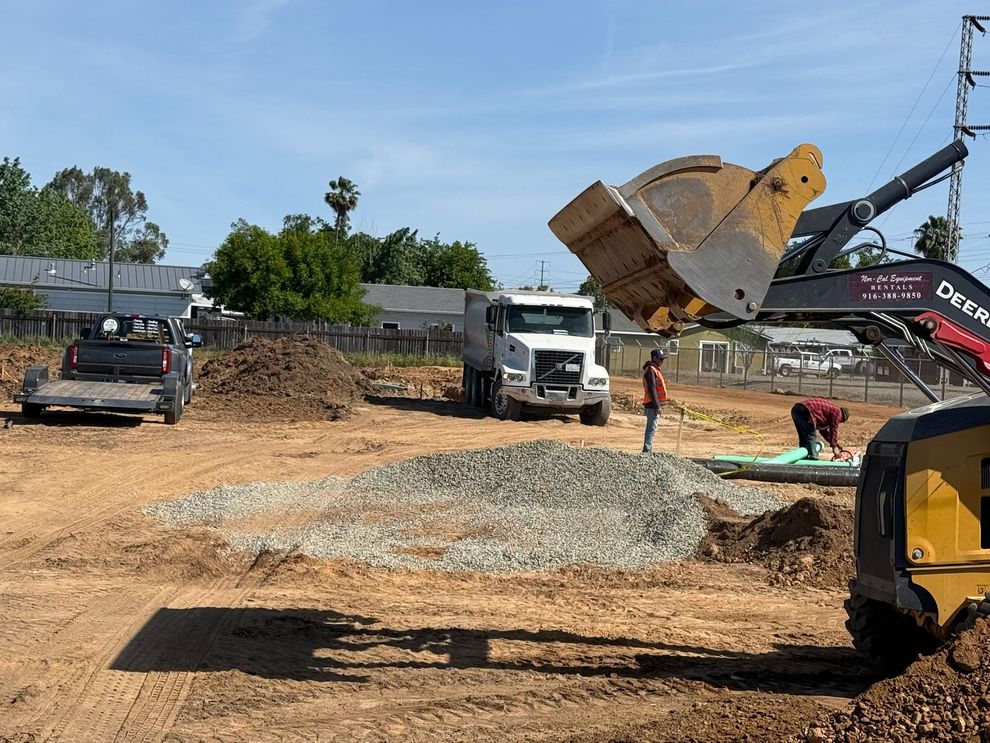 Construction site with excavators and dump trucks moving gravel under a clear blue sky