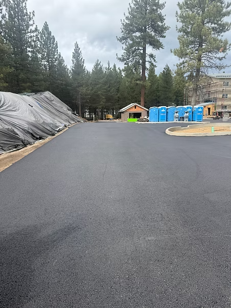 Freshly paved road or lot lined with trees, tarps, and portable toilets at a construction site