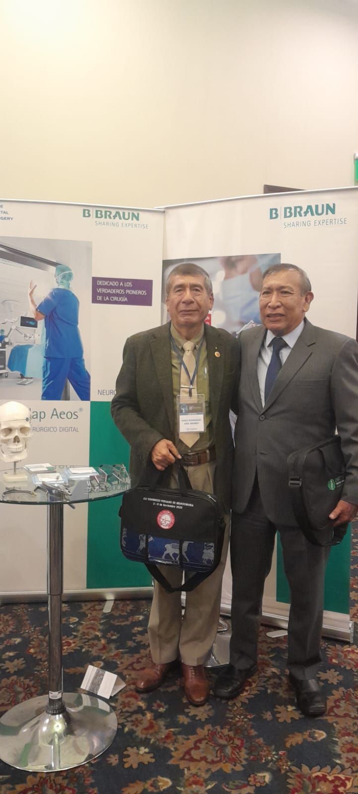 Dos hombres están de pie frente al telón de fondo de una conferencia. Uno sostiene una bolsa.