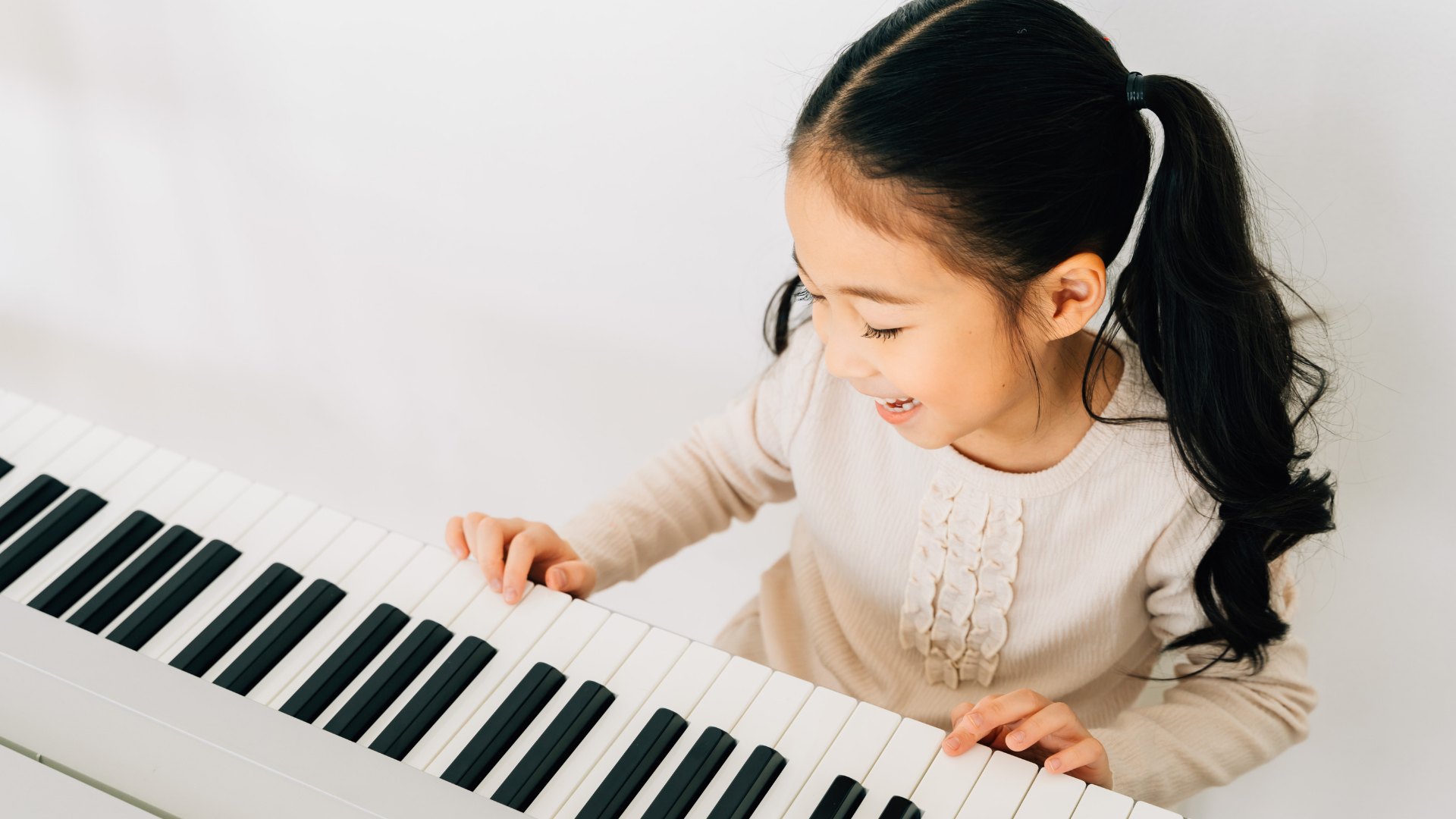 Young child playing a white keyboard piano, smiling and looking down at the keys.