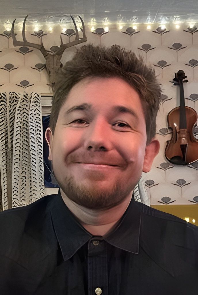 Person smiling in a patterned room with string lights, a violin on the wall, and antlers above.