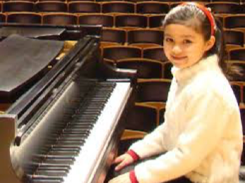 Girl smiling at a grand piano in an empty concert hall