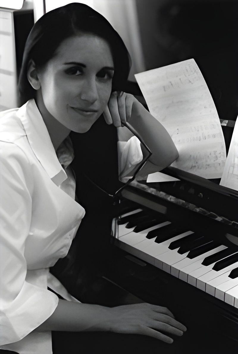 Woman seated at a keyboard piano, resting her head on one hand beside sheet music.