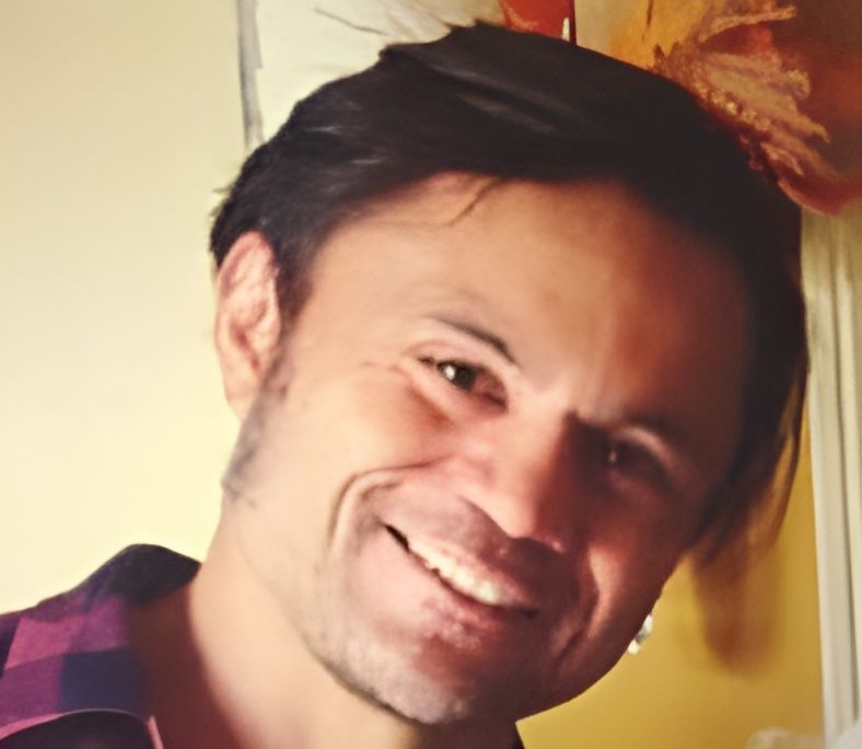 Smiling man with dark hair leaning slightly in warm indoor light