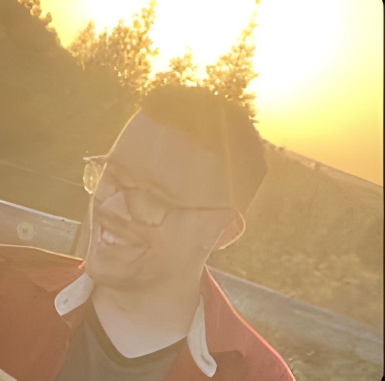 Person wearing glasses and a red jacket smiles in warm sunset light outdoors.