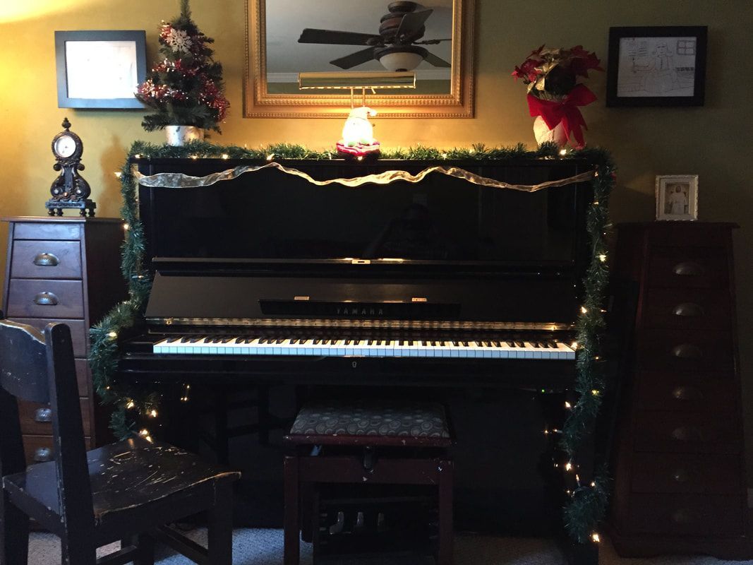 Decorated upright piano in a dim living room with holiday garland, lamp, and mirror above it