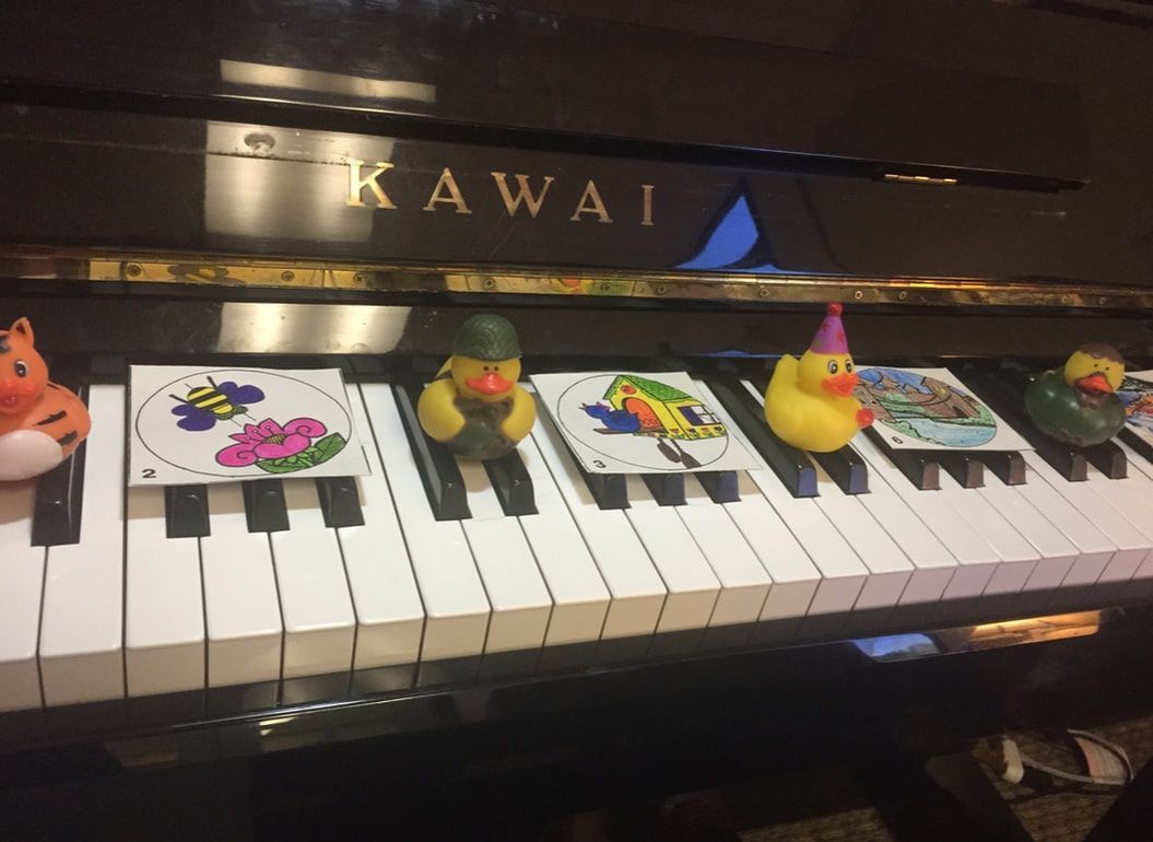 Toy figurines lined up on a Kawai piano keyboard with colorful drawings displayed on the keys.