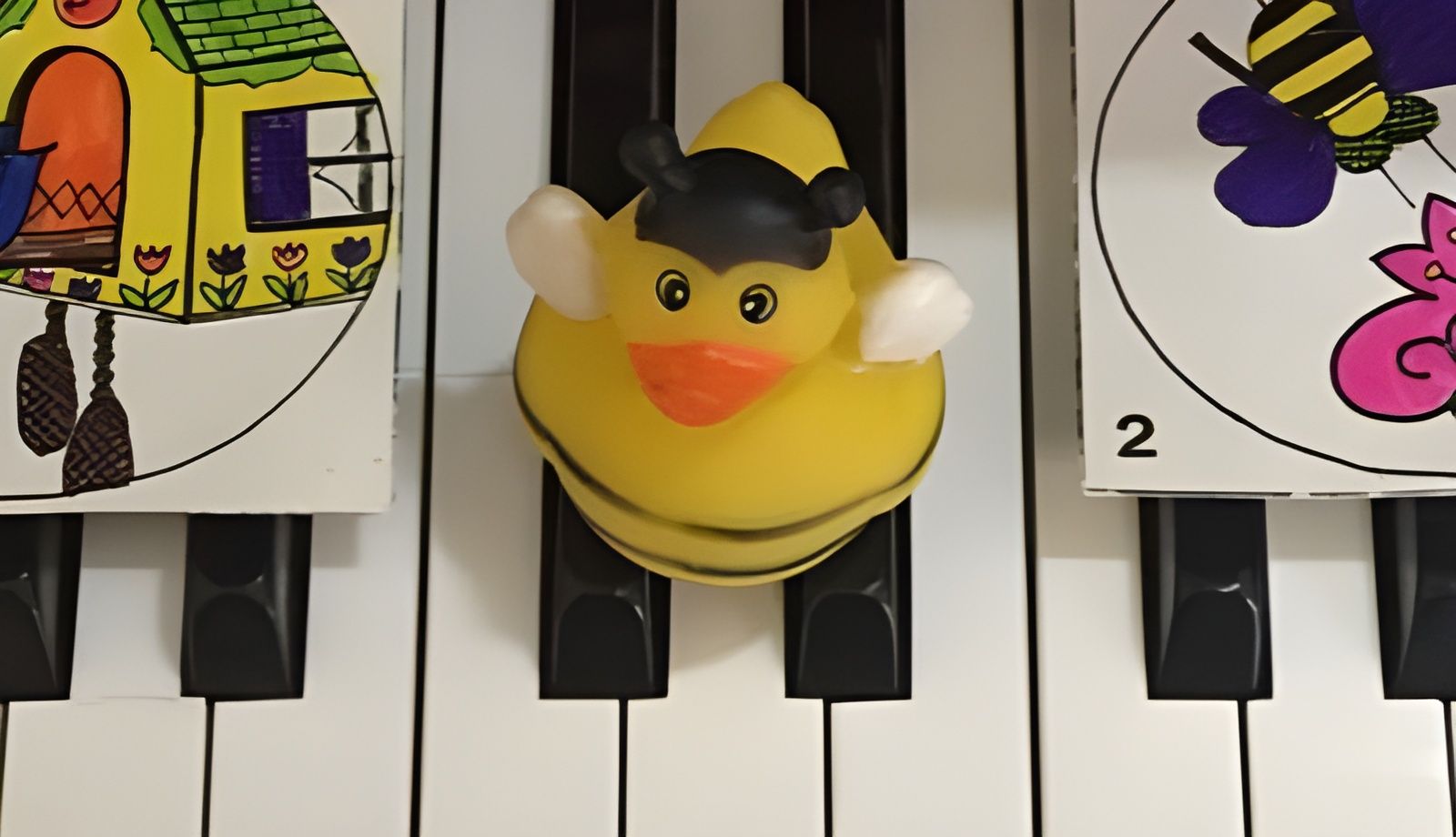 Yellow duck toy on piano keys beside a colorful bee card