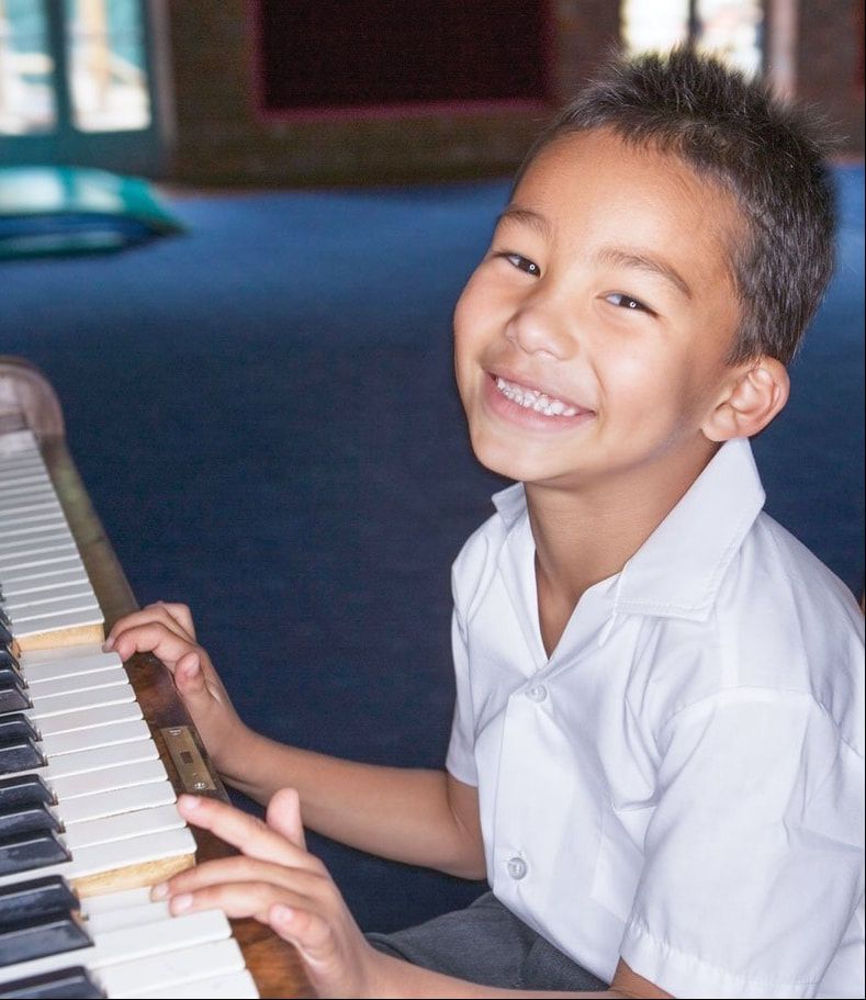 Smiling child playing piano indoors in a white shirt