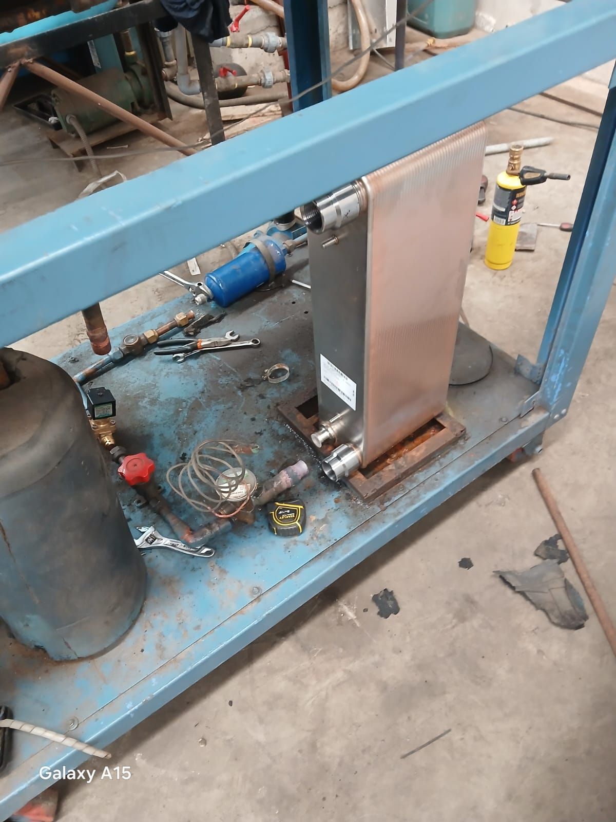Estructura metálica azul con un actuador de acero vertical y mangueras en un taller, con herramientas esparcidas debajo.