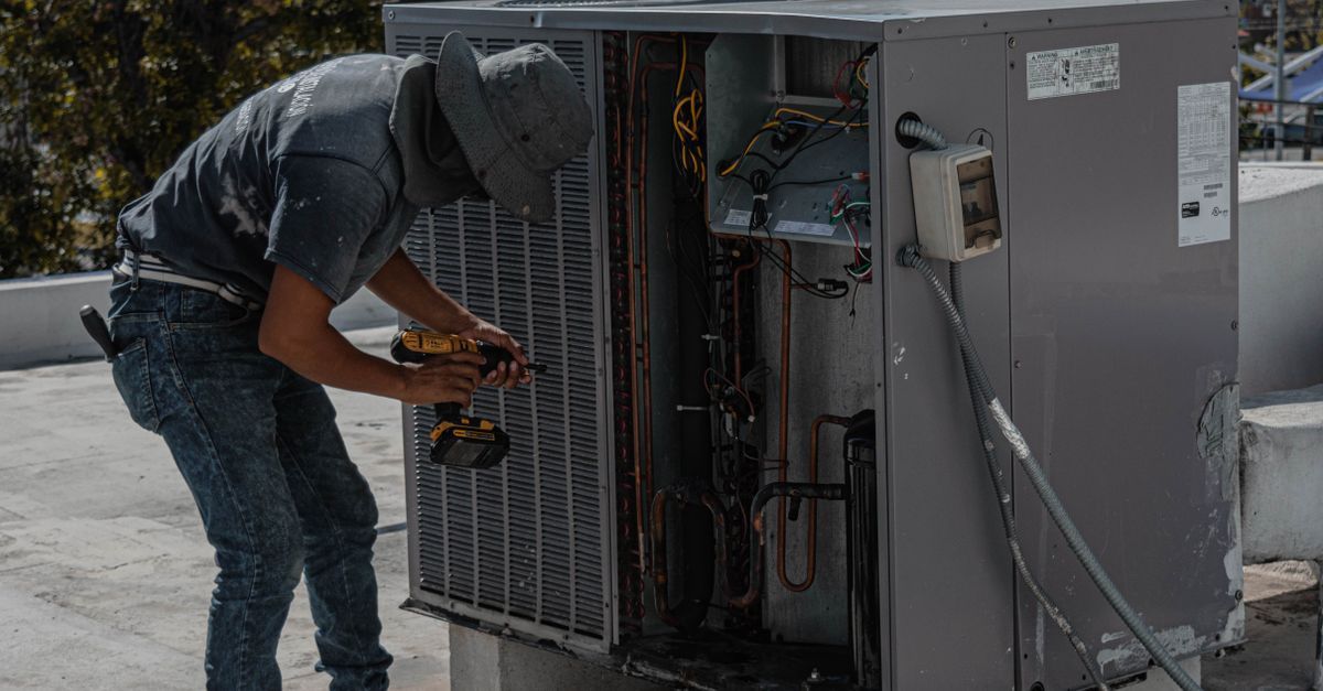 Técnico inspeccionando el lateral abierto de una gran unidad de climatización gris en el exterior.