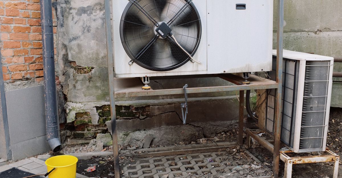 Unidad exterior de climatización con ventilador, montada sobre una estructura metálica junto a una pared de ladrillos