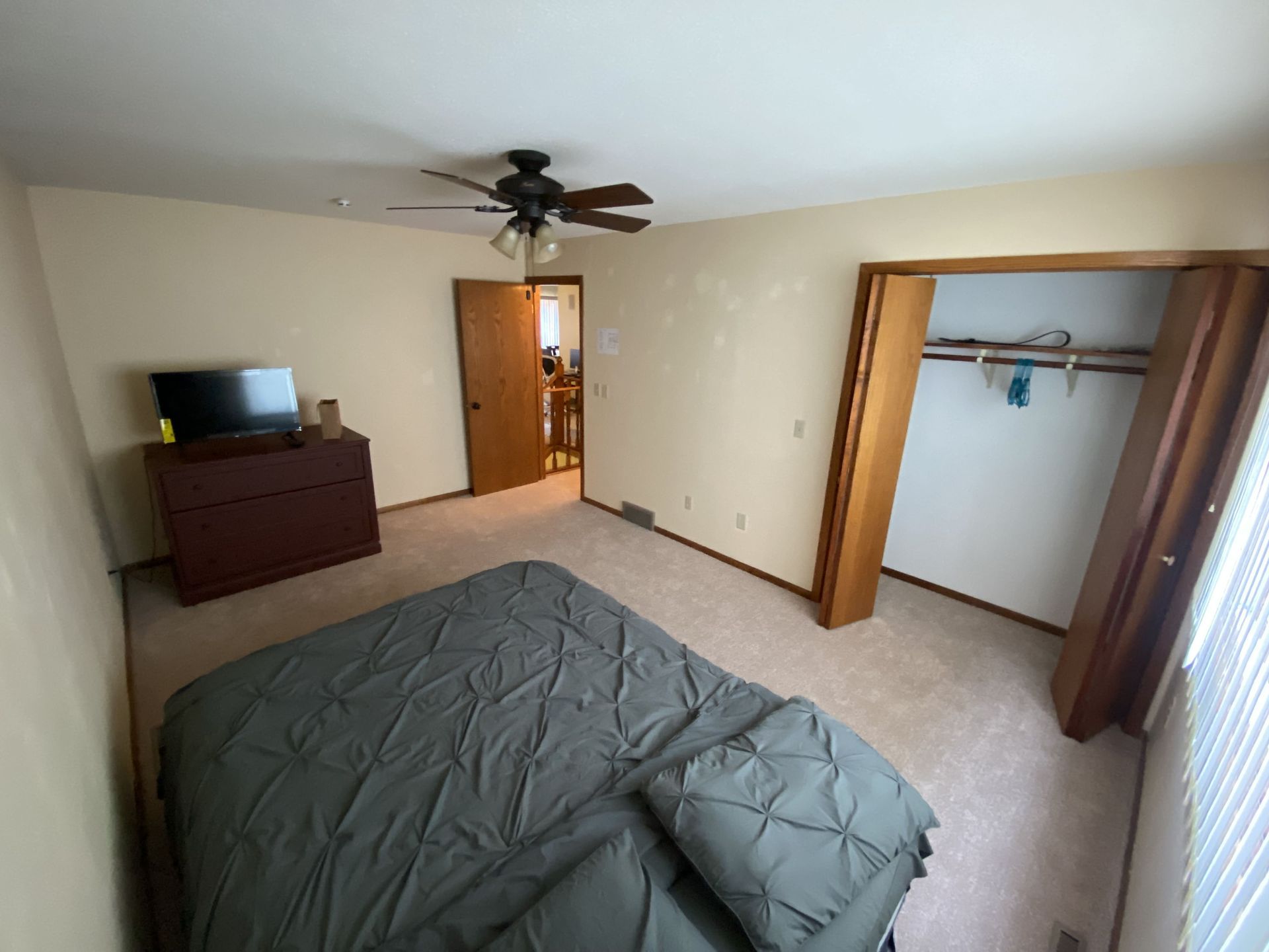 A bedroom with a bed , dresser , television and ceiling fan.