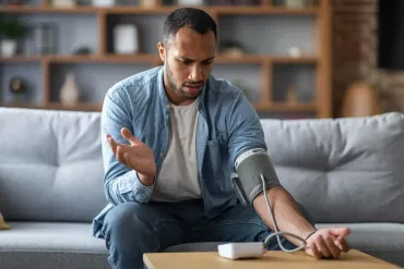 Person checking blood pressure with a cuff while seated on a couch in a living room