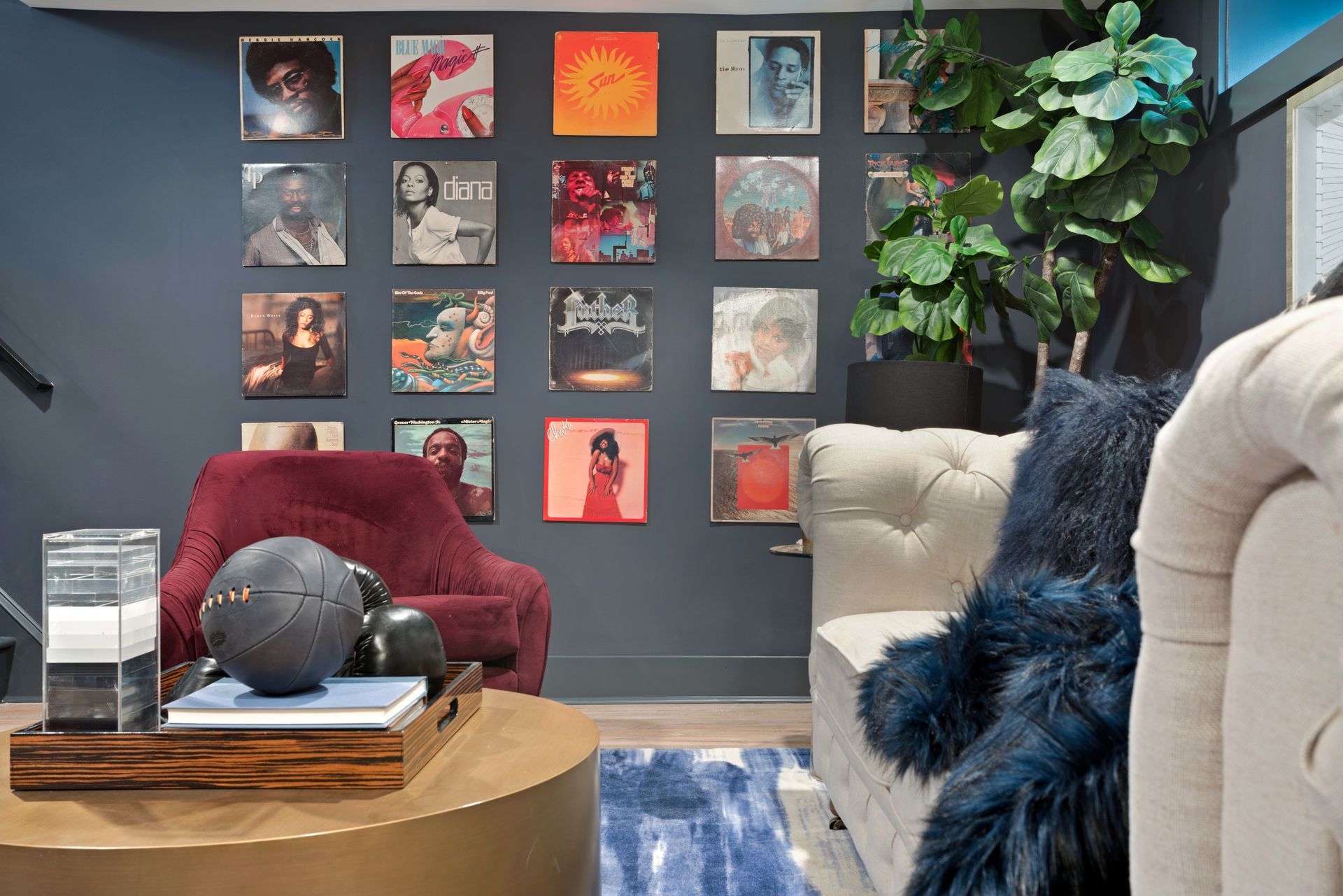 A living room with a couch , chair , coffee table and a wall filled with records.