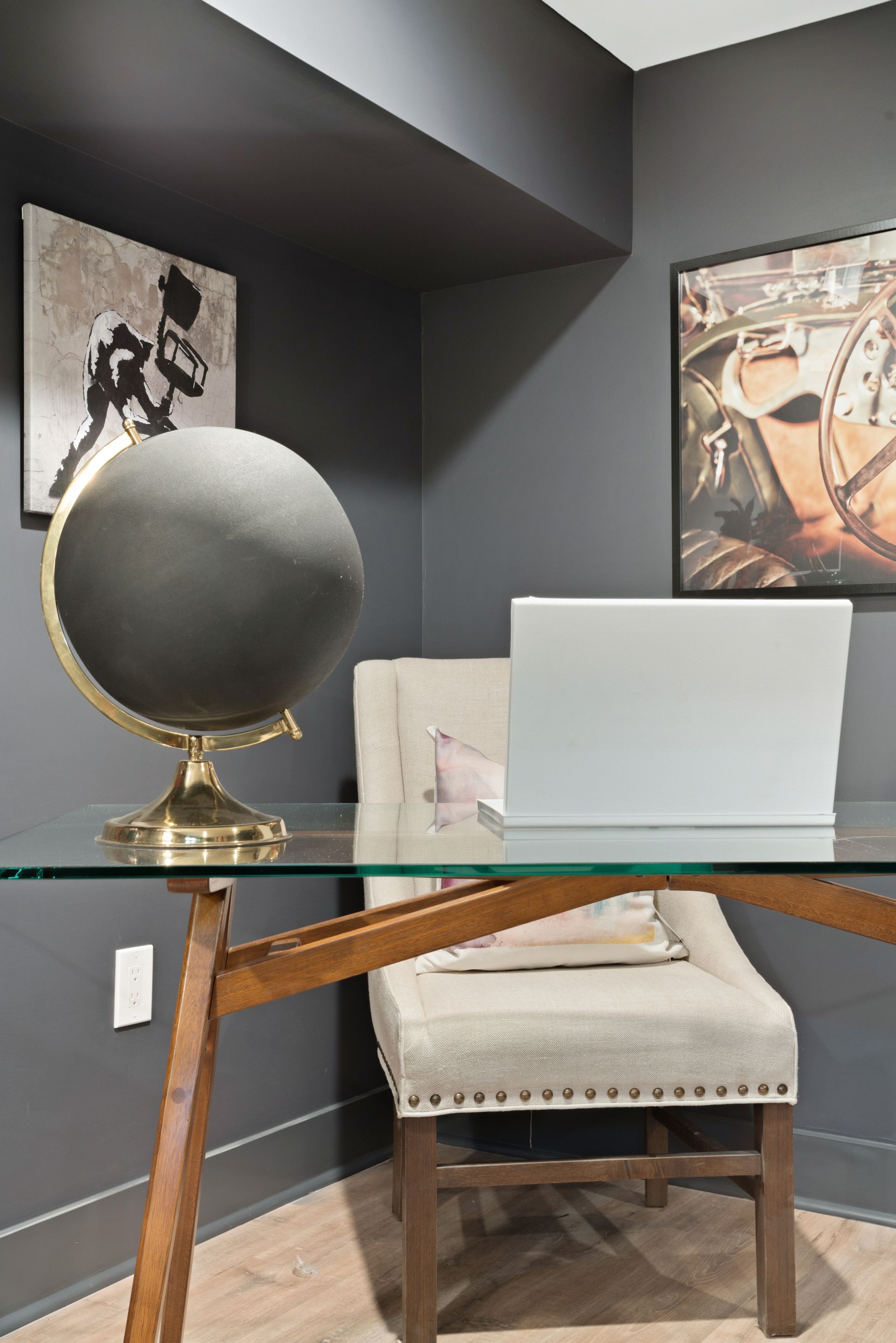 A desk with a laptop on it in a room with a chair and a globe.
