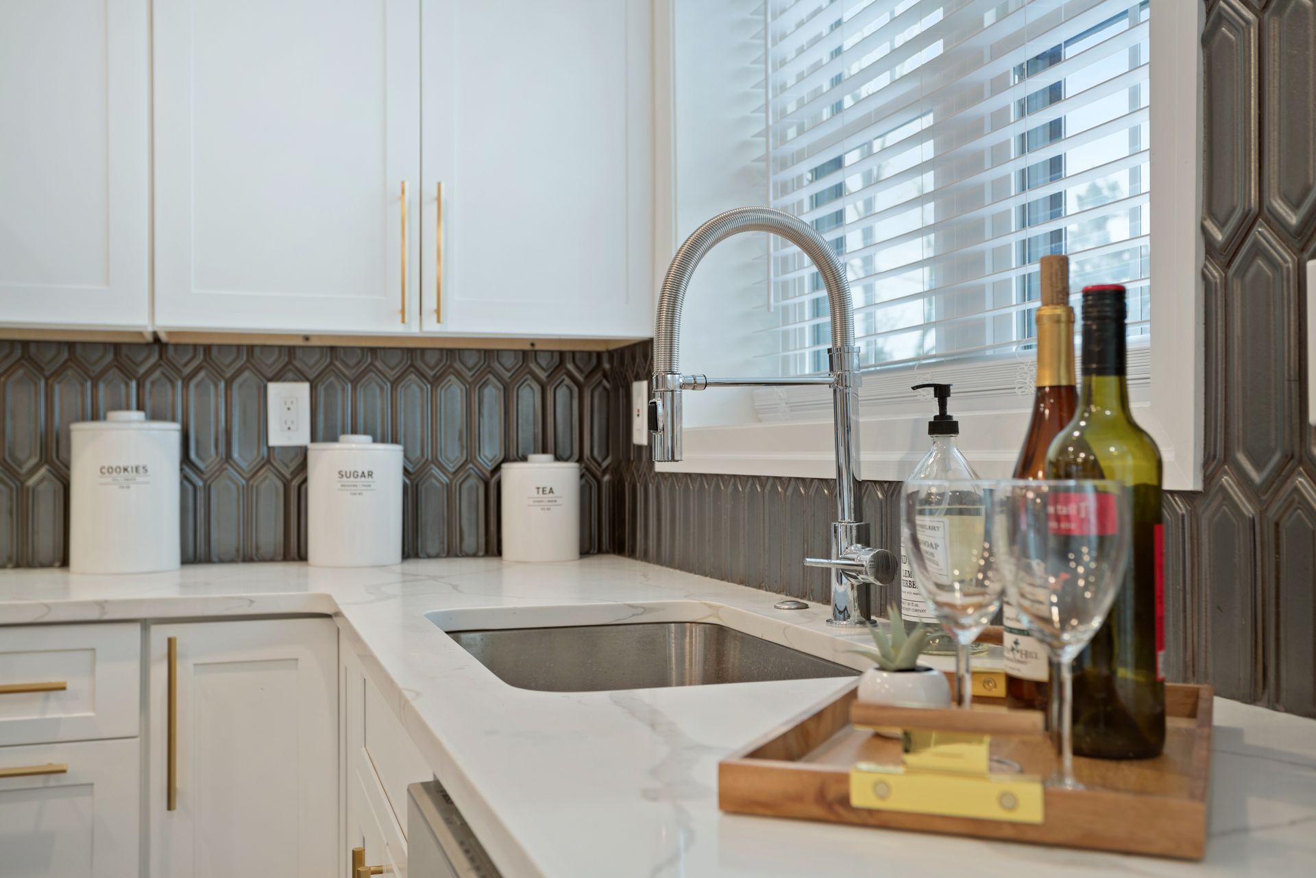 A kitchen with a sink , faucet , bottles of wine and glasses.