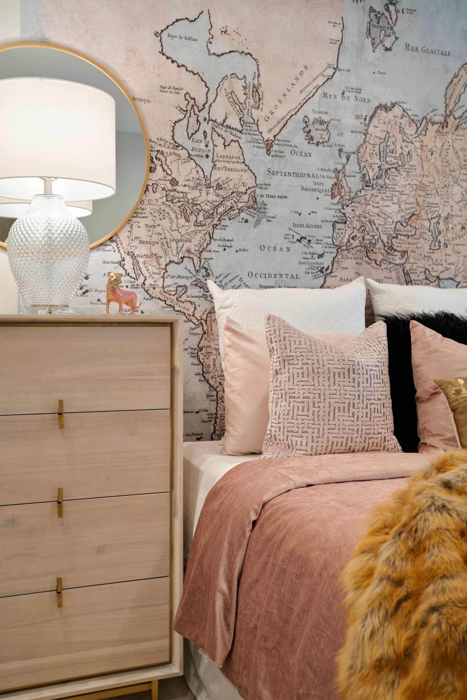 A bedroom with a bed , dresser , mirror and map on the wall.