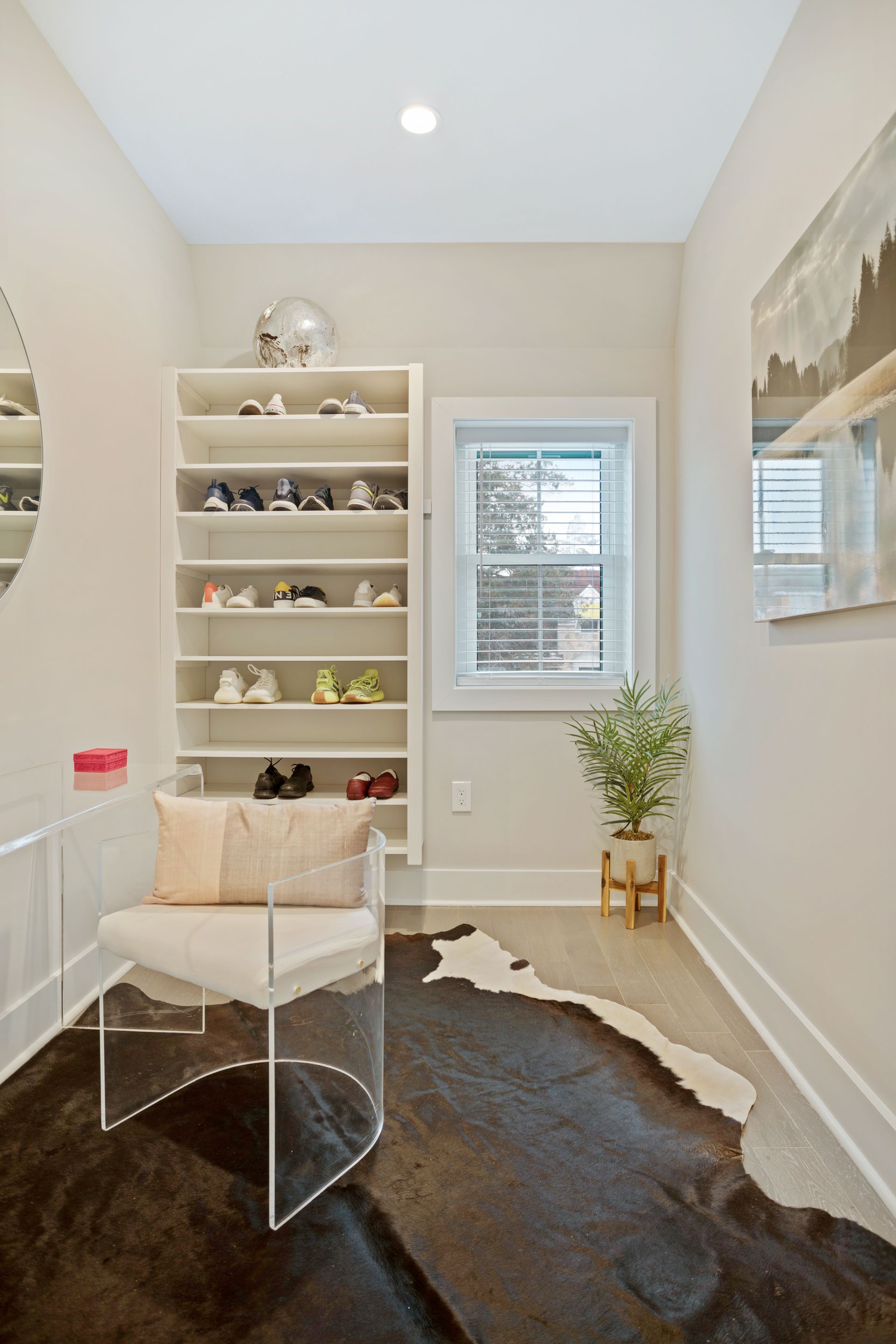 A room with a chair , a rug , a mirror and a shoe rack.