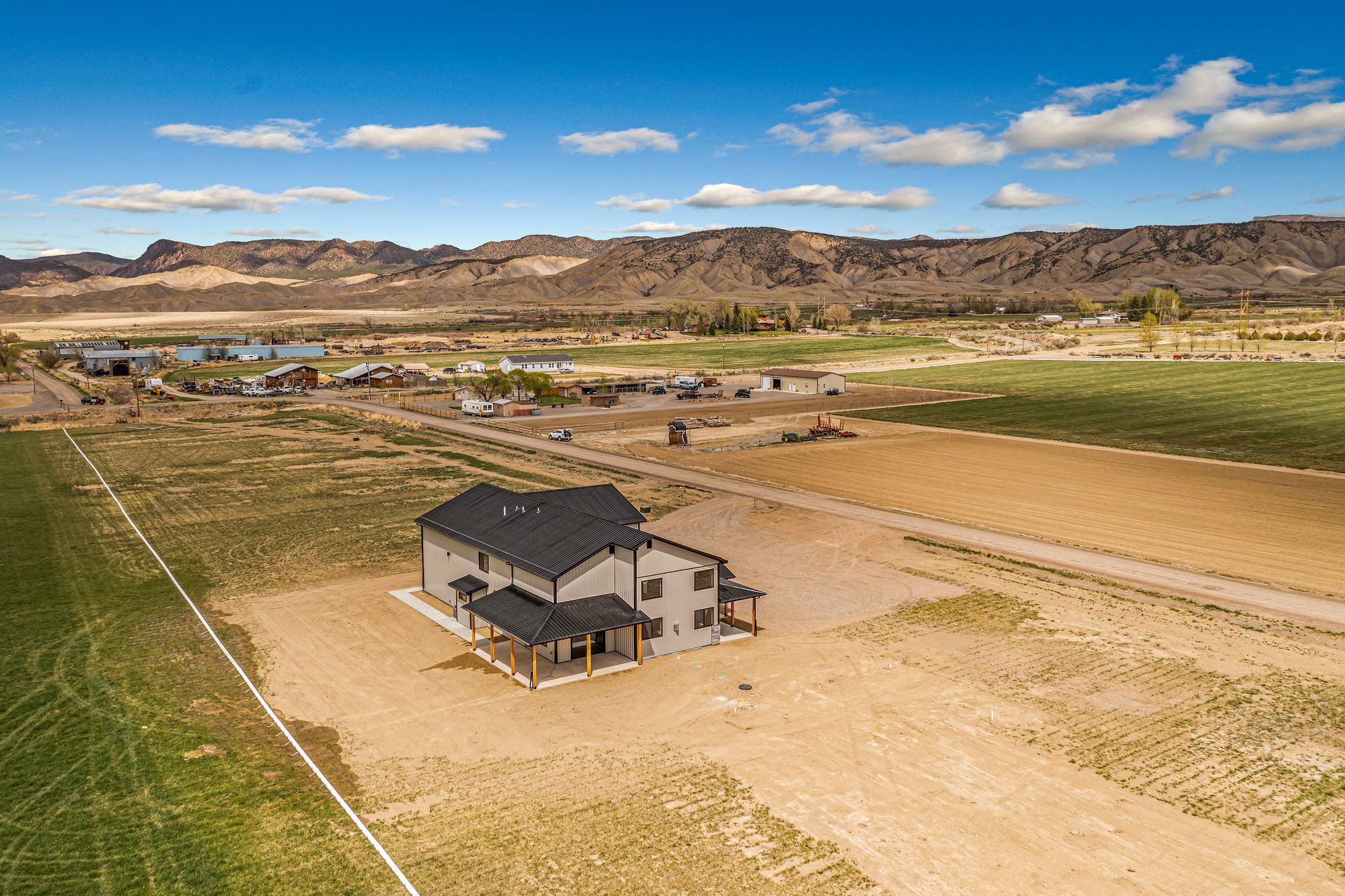 An aerial view of a house in the middle of a field with mountains in the background.