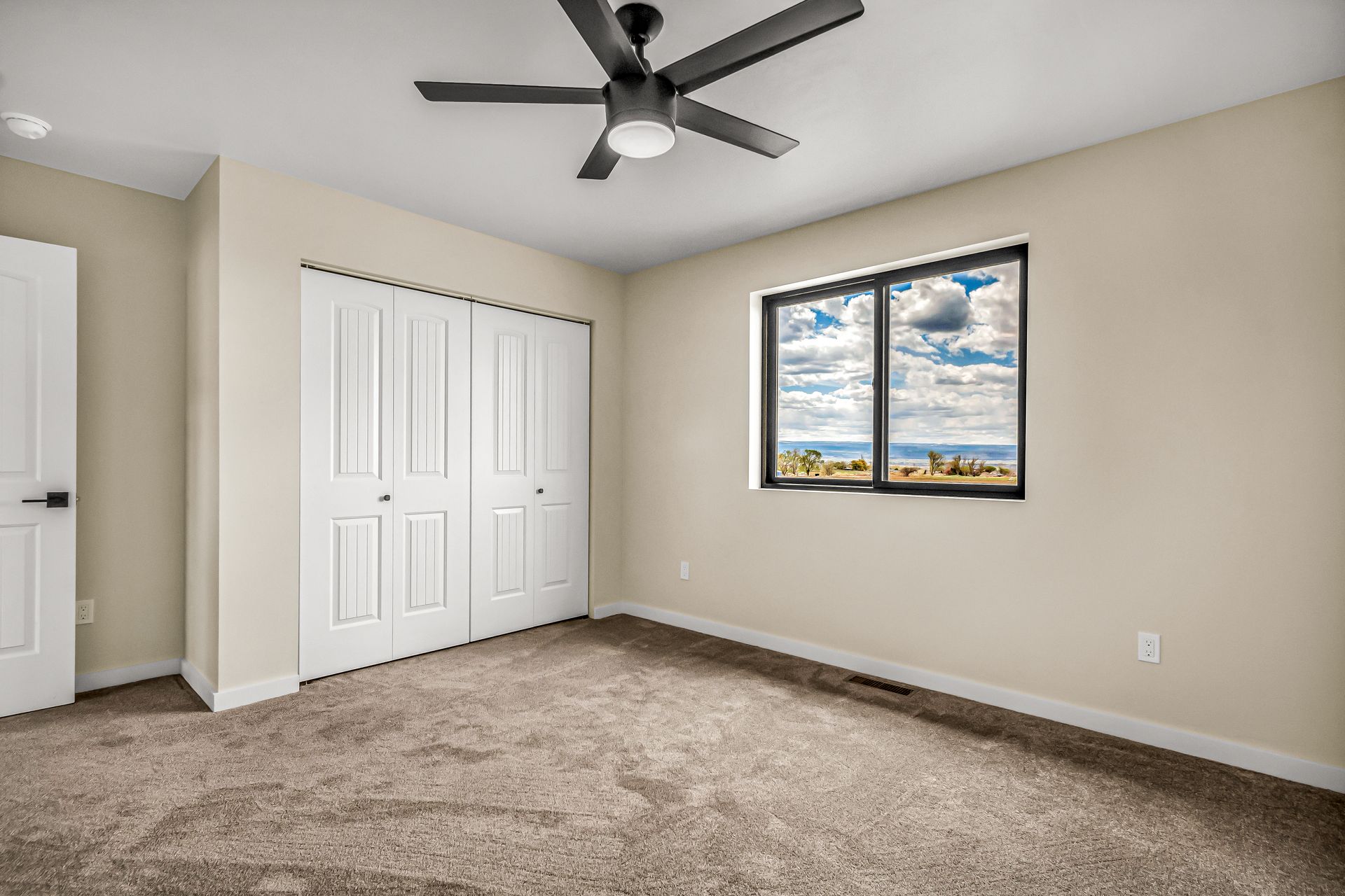 An empty bedroom with a ceiling fan and a window.