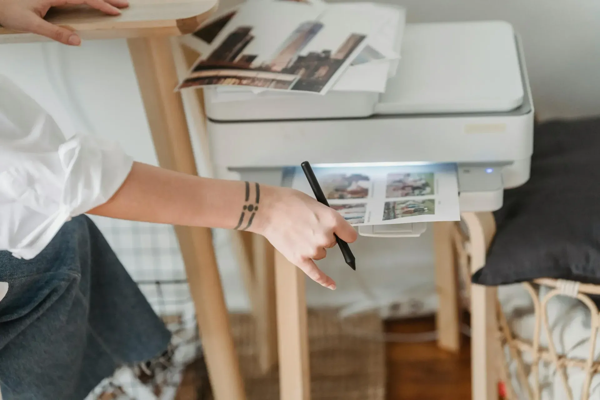 Person reaching into a printer, retrieving printed photos. Printer on a wooden table.