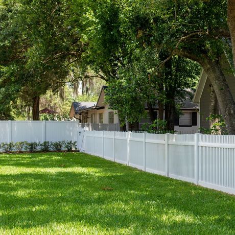 A white picket fence surrounds a lush green yard in front of a house.