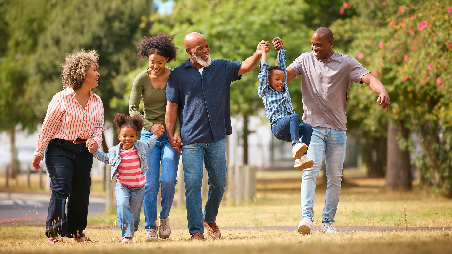 Family walking together in a park, smiling and holding hands under blooming trees.