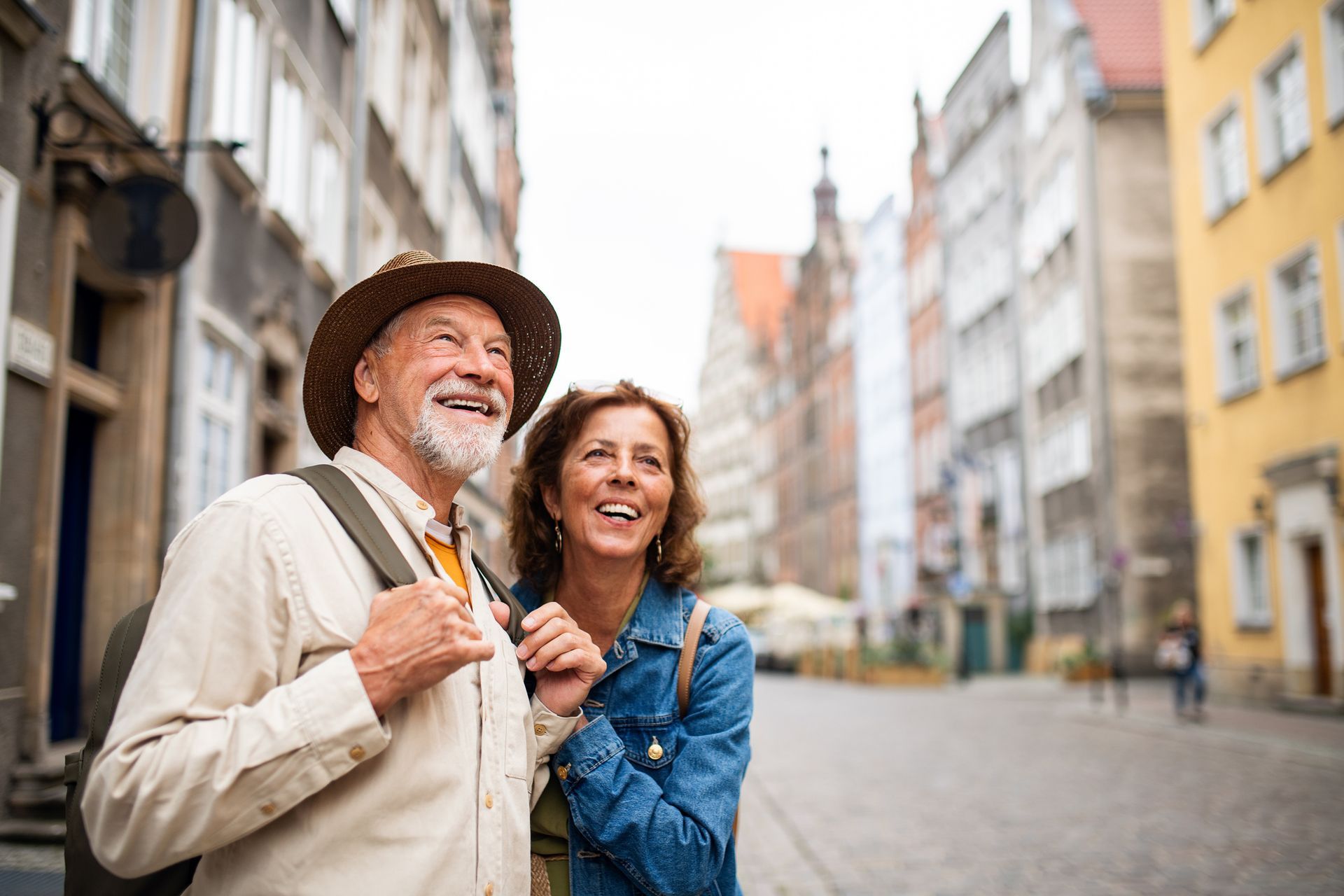 Two smiling travelers with backpacks on a quiet cobblestone street in a European city