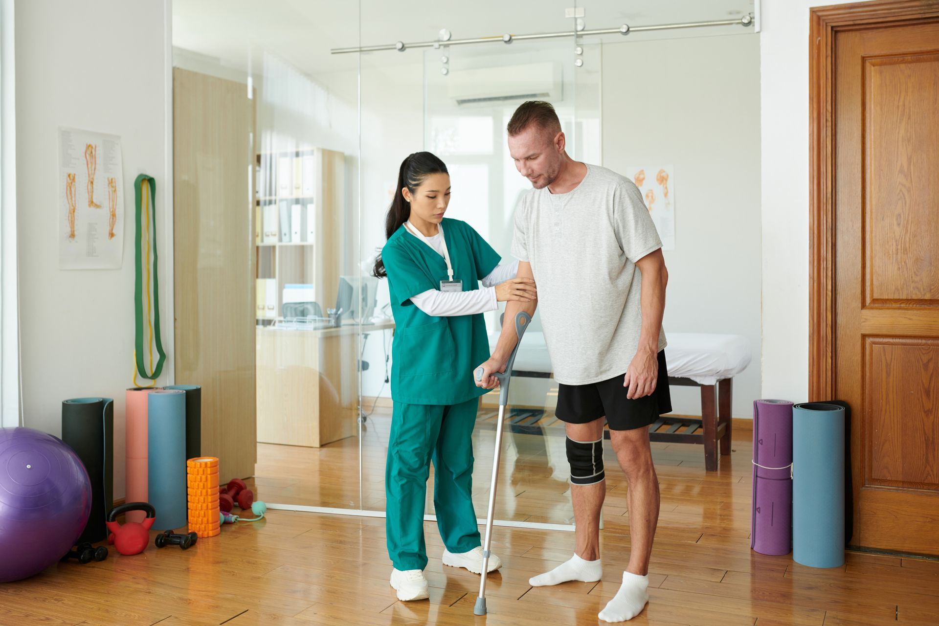 Physical therapist helping a man exercise with a cane in a bright studio, with yoga mats and exercise balls nearby