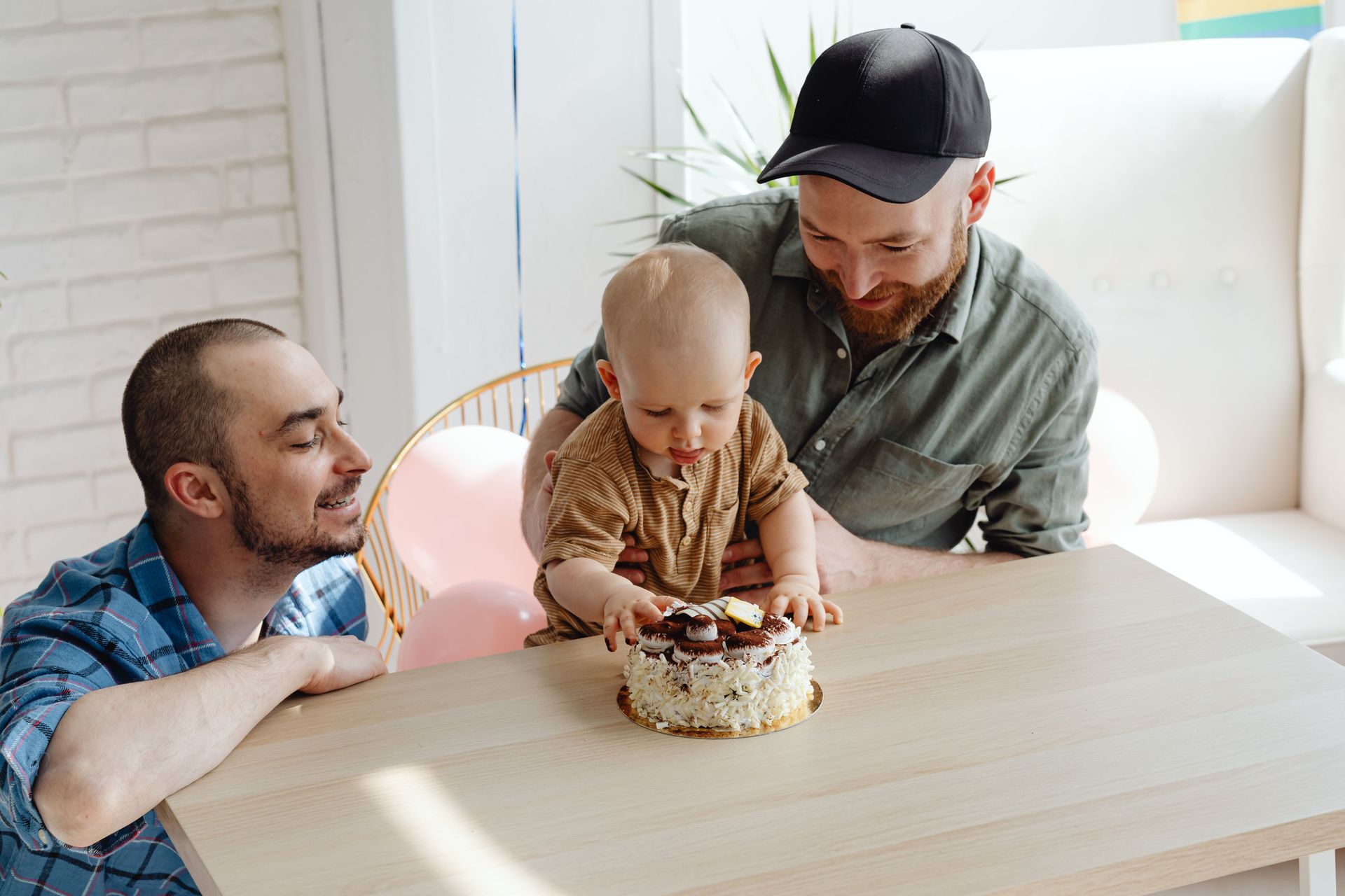 Three people gathered around a table, helping a child blow out a birthday cake candle.