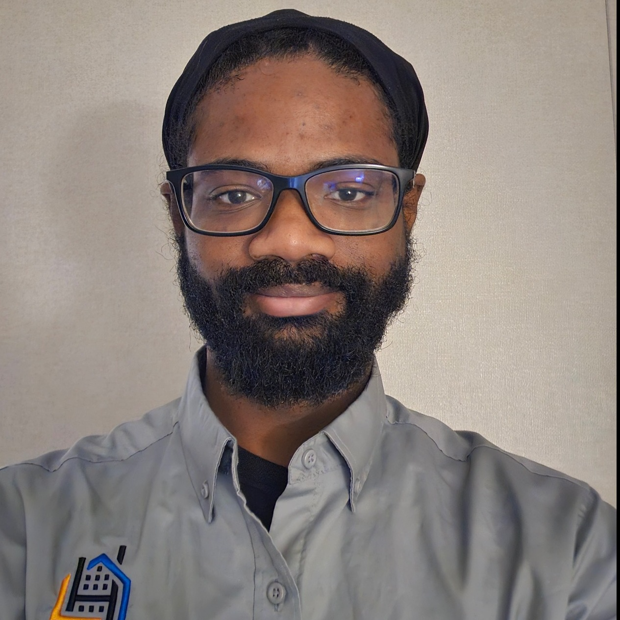 Man with beard wearing a black t-shirt with a logo, smiling.