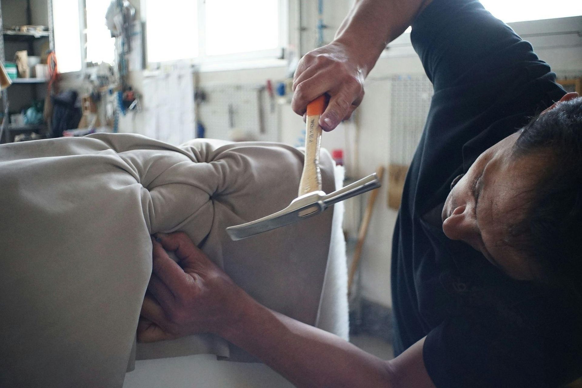 Person upholstering furniture, using a hammer to secure fabric. Workshop setting.
