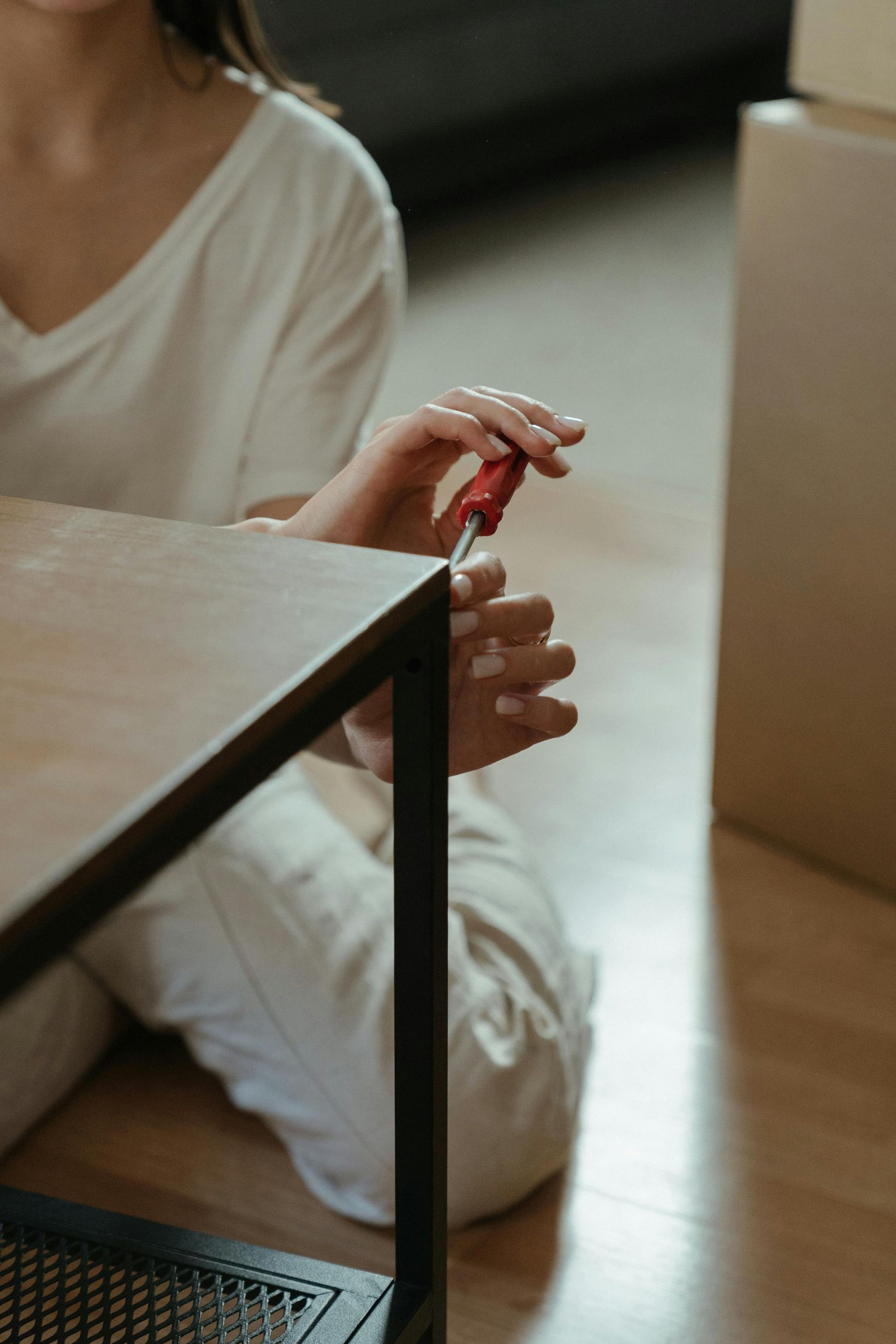 Person assembling furniture with a screwdriver, sitting on the floor by a table.
