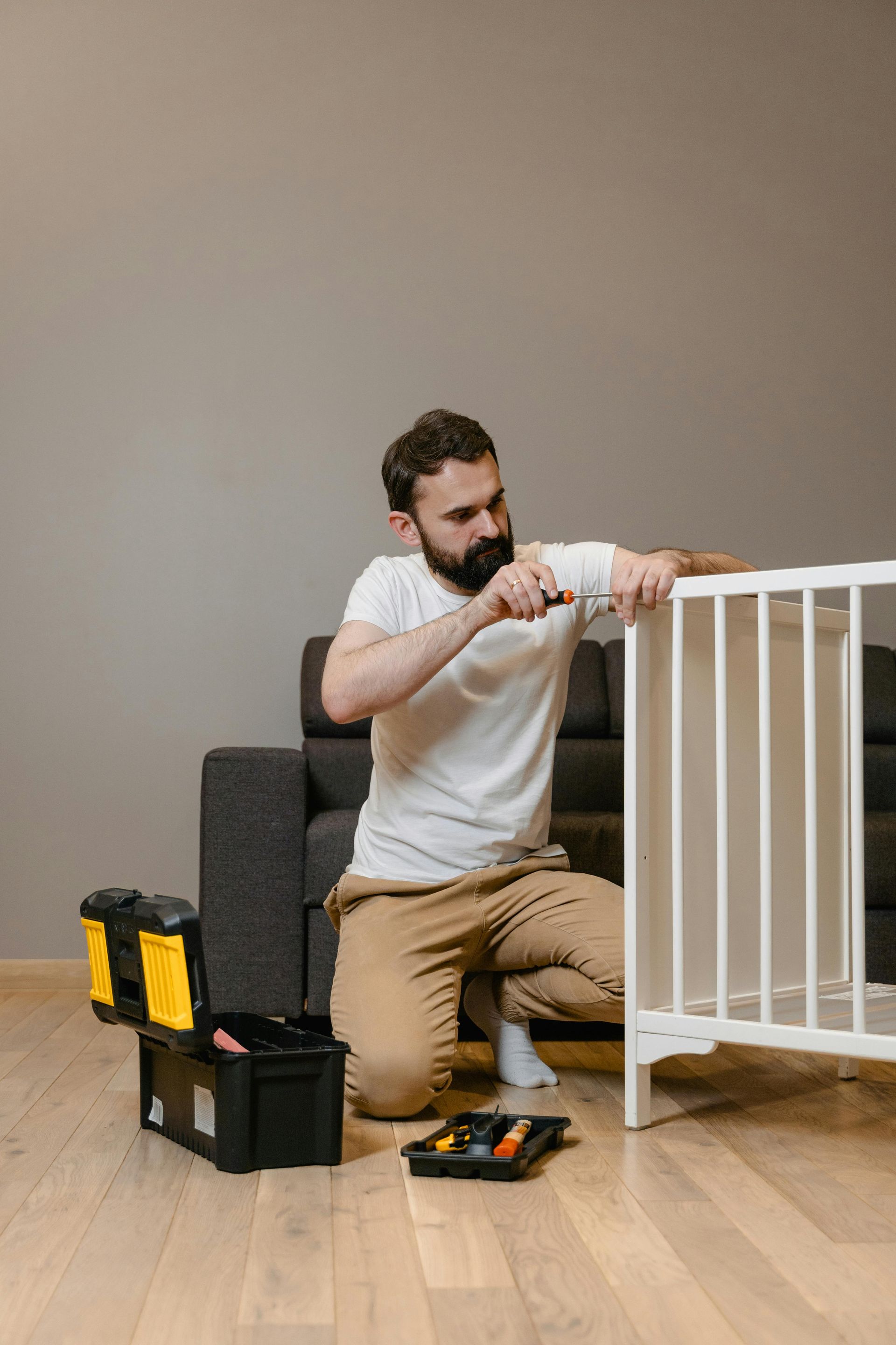 Man assembling a white crib with a screwdriver, a toolbox nearby, indoors.
