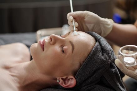 Facial treatment with a woman lying back as gloved hands apply serum to her forehead