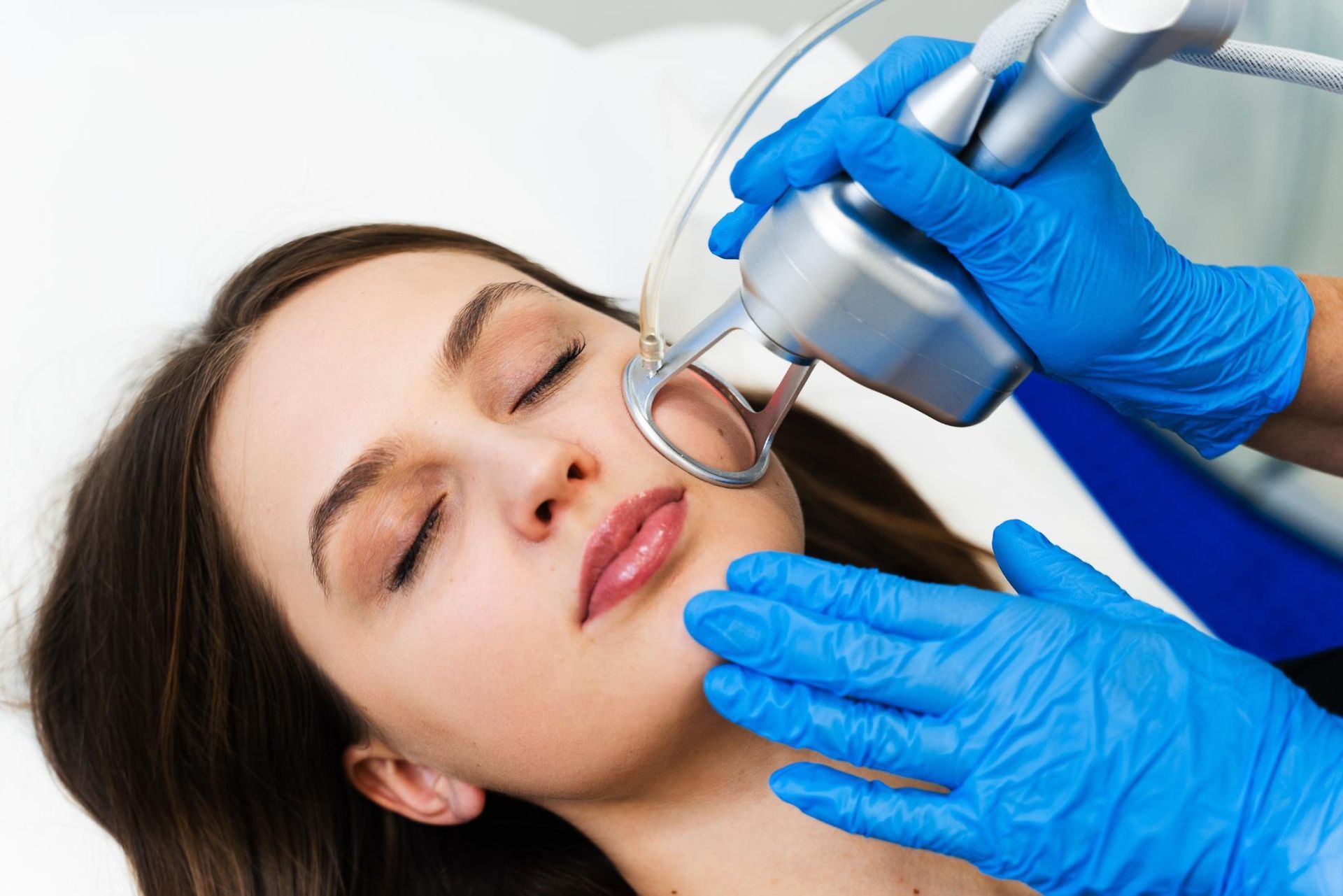 Gloved clinician performing a facial skin treatment with a handheld device on a relaxed patient
