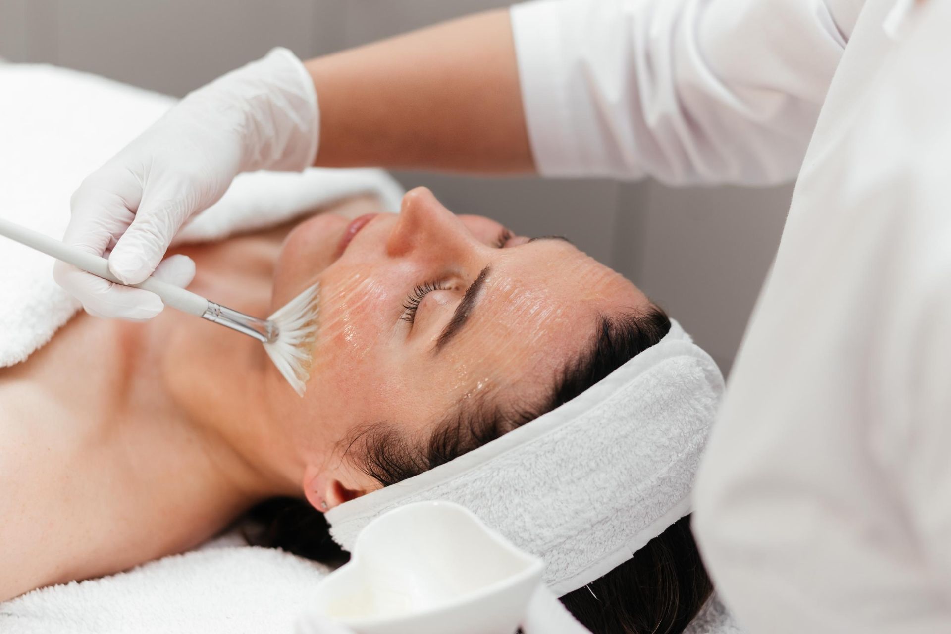 Facial treatment with a brush on a relaxed client wearing a headband and gloves